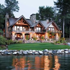 a large house sitting on top of a lush green hillside next to a lake in front of a forest