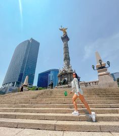 a woman is walking down some steps in front of a statue and buildings on the other side