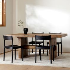 a dining table with four chairs and a vase on the top, in front of a white wall