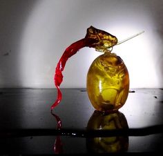 a yellow glass vase with a red liquid pouring out of it's top, on a black surface