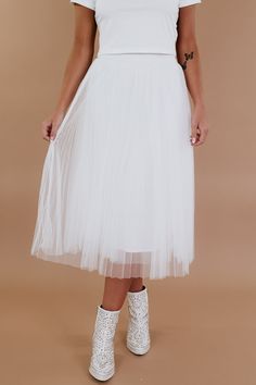 a woman wearing white shoes and a tulle skirt is standing in front of a beige background