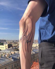 a man with a tattoo on his arm standing in front of a cityscape