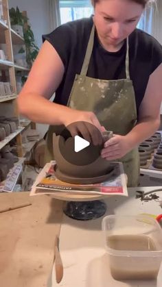 a woman in an apron is decorating a clay pot on a table with pottery