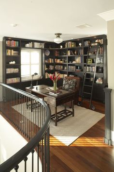 a living room filled with lots of bookshelves next to a stair case in front of a window