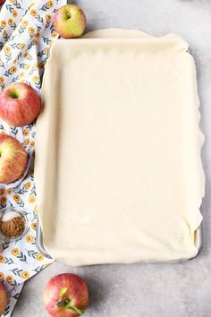 an uncooked apple pie sitting on top of a table next to some apples