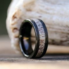 a wooden ring with black and white wood inlays the center, resting on a piece of driftwood