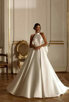 a woman in a white wedding dress standing on the floor with her hands behind her back