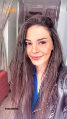 a woman with long brown hair and blue shirt smiling at the camera while wearing a leather jacket