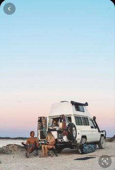 two people sitting in chairs next to a camper van on the beach at sunset