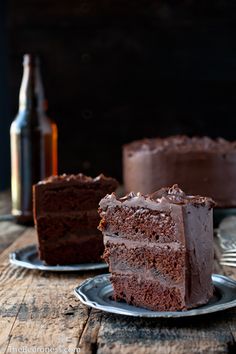 a slice of chocolate cake on a plate next to a beer bottle and spoons