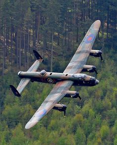 an old airplane flying in the air over some trees