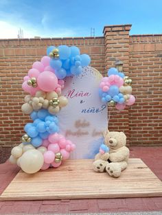 a teddy bear sitting on top of a wooden table next to balloons and a sign