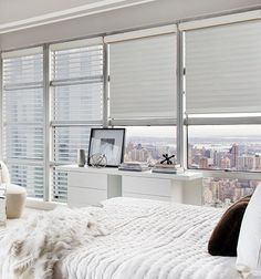 a bedroom with white furniture and large windows overlooking the cityscape in the distance