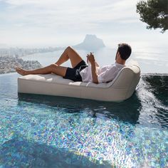 a man sitting on an inflatable lounge chair next to the pool drinking a beverage