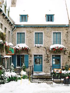 an old stone building covered in snow with blue shutters and red flowers on the windows