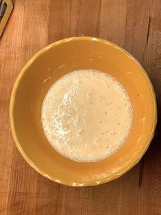 a yellow bowl filled with liquid on top of a wooden table