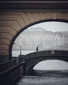 a man standing on the edge of a bridge next to a body of water with buildings in the background