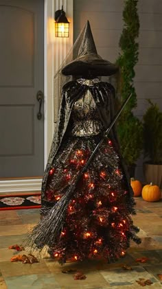 a lighted halloween tree with a witch hat and broom on the front porch, surrounded by pumpkins