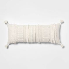 a white pillow with tassels on the front and back, against a white background