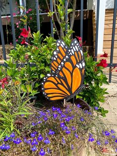 an orange and black butterfly sitting on top of purple flowers in front of a fence