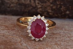 an oval shaped ruby and diamond ring on top of a stone slab, with small white diamonds around the band