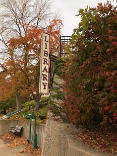 there is a sign that says library on the side of the road in front of some trees