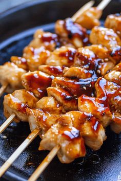 chicken skewers are being cooked on a black plate with toothpicks in them