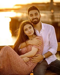 a man and woman are sitting on a bench near the water with their arms around each other