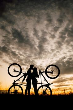 two people standing next to each other with bikes on their shoulders and the sky in the background