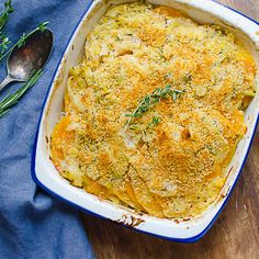 a casserole dish with cheese and herbs in it on a wooden table next to a spoon