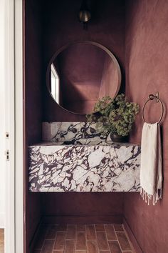 a bathroom with a marble counter top and round mirror above the sink, along with a plant