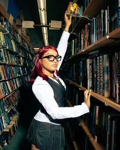 a woman with red hair and glasses standing in front of a book shelf filled with books