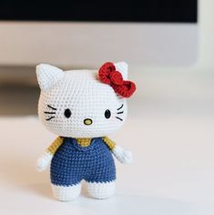 a crocheted hello kitty doll with a red bow on her head standing in front of a computer monitor