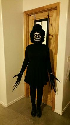 a person in a skeleton mask and black dress standing next to an open door with their hands out