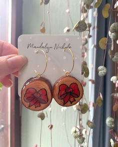 There's nothing better than a unique twist to a classic look with these red ribbon earrings. These wooden earrings are completely unique and handmade with love! Showing off the vibrant red ribbons, these red ribbon earrings would be a great addition to your earring collection ⭐ 🌟 Features: Material: Wood, Resin, Acrylic Paint, and Surgical Steel Size: approximately 6 cm long, and 3 cm wide Shape: Circle/Oval Color: red, black, brown Coating: Natural resin for water resistant durability  Hardwar Red Hoop Earrings For Gift, Hoop Earrings For Valentine's Day Gift, Handmade Red Hoop Earrings As Gift, Elegant Hand Painted Red Earrings, Red Hand Painted Round Earrings, Retro Red Round Earrings, Brown Wood Drop Earrings, Ribbon Earrings, Unique Brown Wooden Earrings