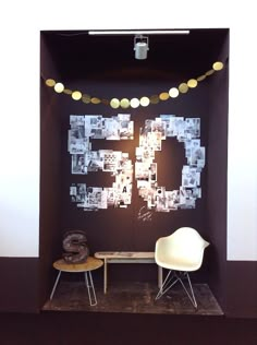 two chairs and a table in front of a wall with pictures on it, some lights strung from the ceiling