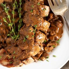 a white plate topped with meat covered in gravy and garnished with parsley