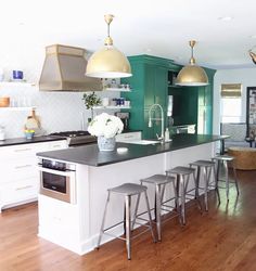 a kitchen with green cabinets and gold pendant lights over the island, white countertops and stools