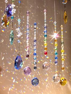 many different colored beads hanging from strings in front of a white wall with light shining through them