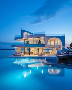 a large swimming pool in front of a modern house at dusk with the lights on