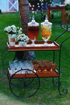 a wooden table topped with drinks and glasses on top of a grass covered field next to a tree