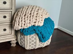 a basket that has some blankets on top of it next to a dresser with drawers