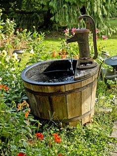 an old fashioned water pump in a wooden barrel filled with water and surrounded by wildflowers