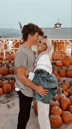 a man and woman standing next to each other in front of pumpkins