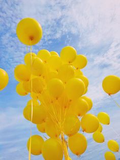 a bunch of yellow balloons floating in the air with blue sky and clouds behind them