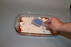 a person is spreading sauce on top of food in a plastic container with a spatula