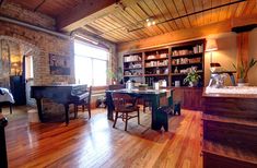 a living room filled with furniture and a piano in front of a window on top of a hard wood floor