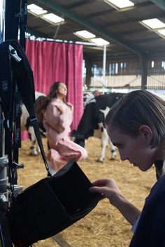 a woman looking at something in her hand while standing next to some cows on the ground