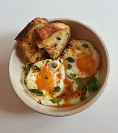 two fried eggs in a bowl with toast on the side and garnished with green leaves