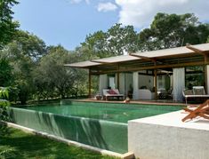 an outdoor swimming pool surrounded by lush green trees and grass, with lounge chairs around it